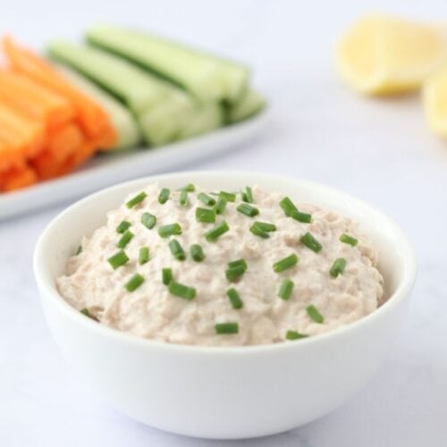 Bowl of easy summer dip with chives, veggies, and lemon wedges in the background.