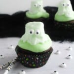 Candy ghost atop green frosting on a chocolate cupcake.