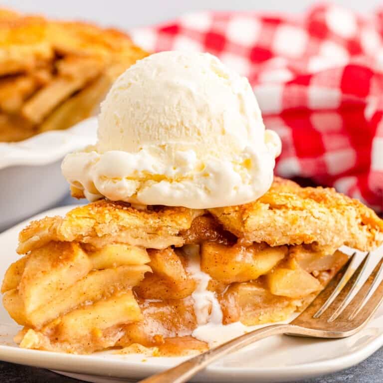 Close up shot of apple pie with vanilla ice cream on top sitting on a white plate.