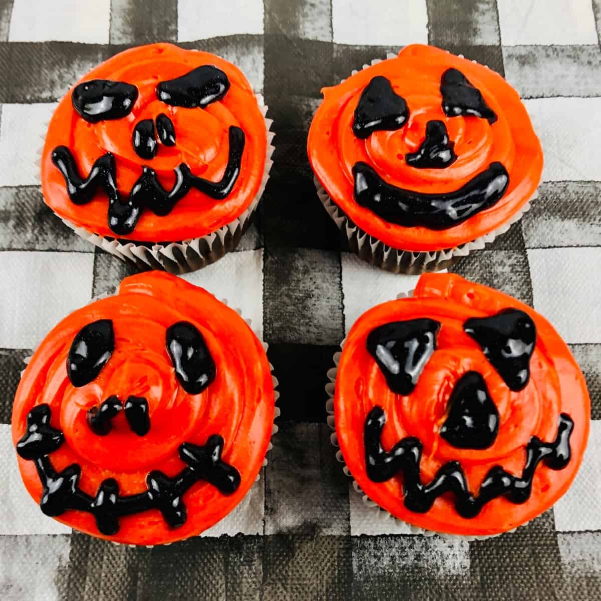 Four cupcakes decorated to look like a jack-o-lantern with orange and black frosting.