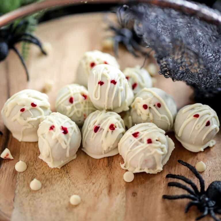 Mummy themed pumpkin truffles covered in white chocolate with plastic spider decorations.