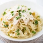 A plate of chicken alfredo pasta topped with fresh parsley.