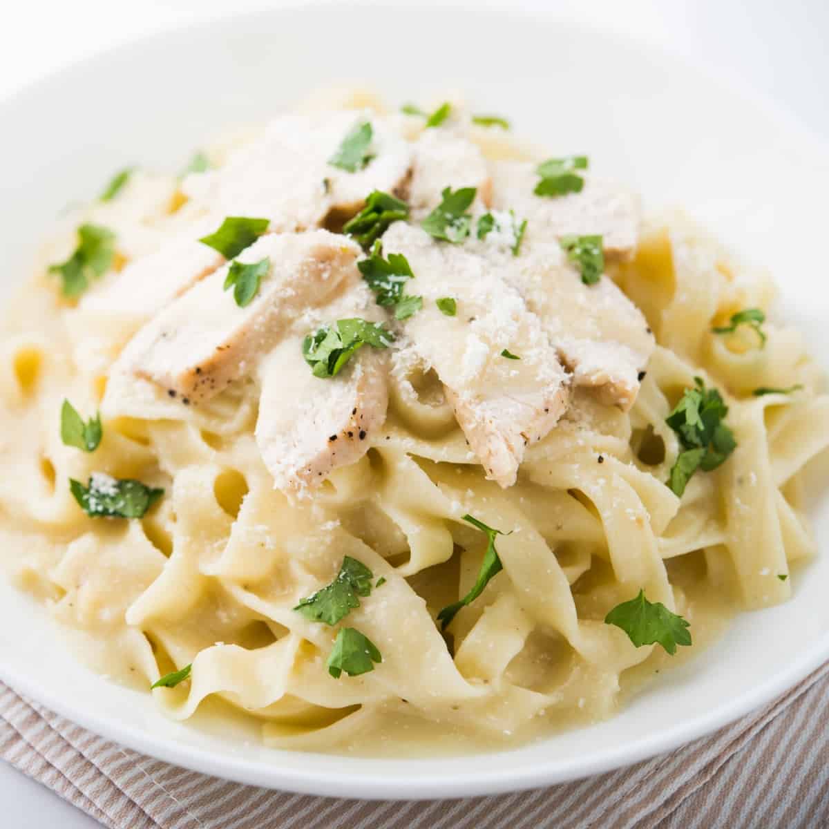 A plate of chicken alfredo pasta topped with fresh parsley.