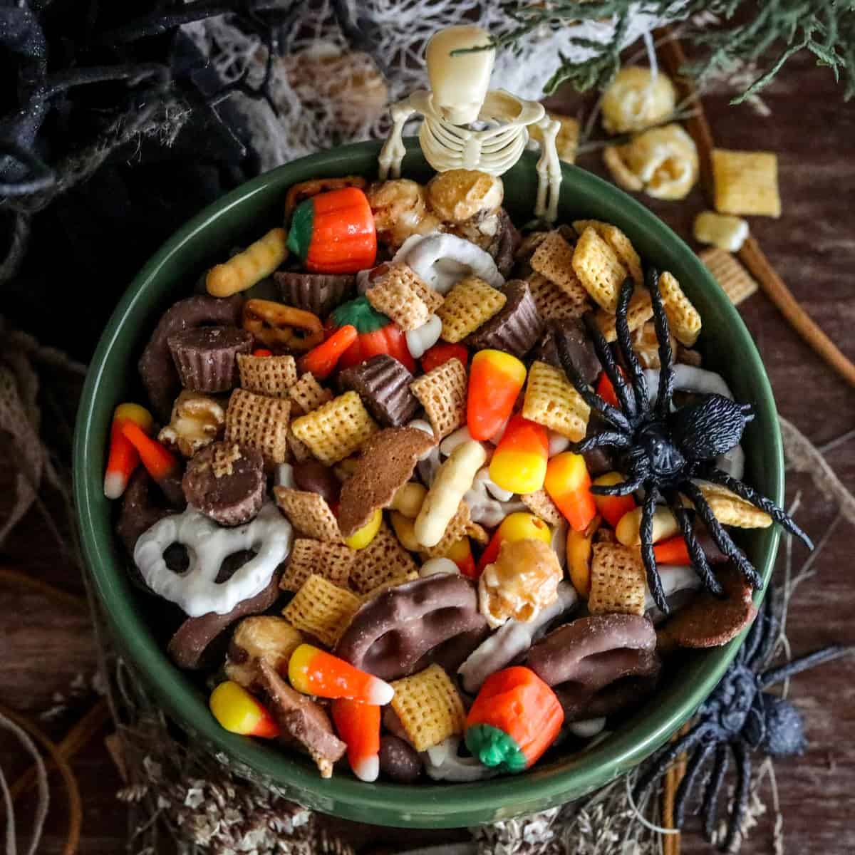 A bowl of fall Chex party snack mix with a skeleton and spider decoration inside.