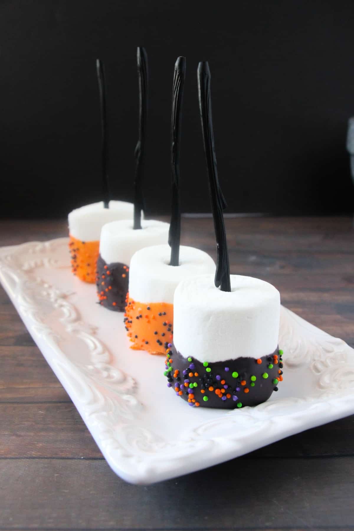 Hallowwen themed large marshmallow pops with half coated candy melts with sprinkles on a white platter.