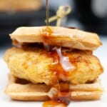 Chicken and waffles sitting on a white plate drizzled with maple syrup.