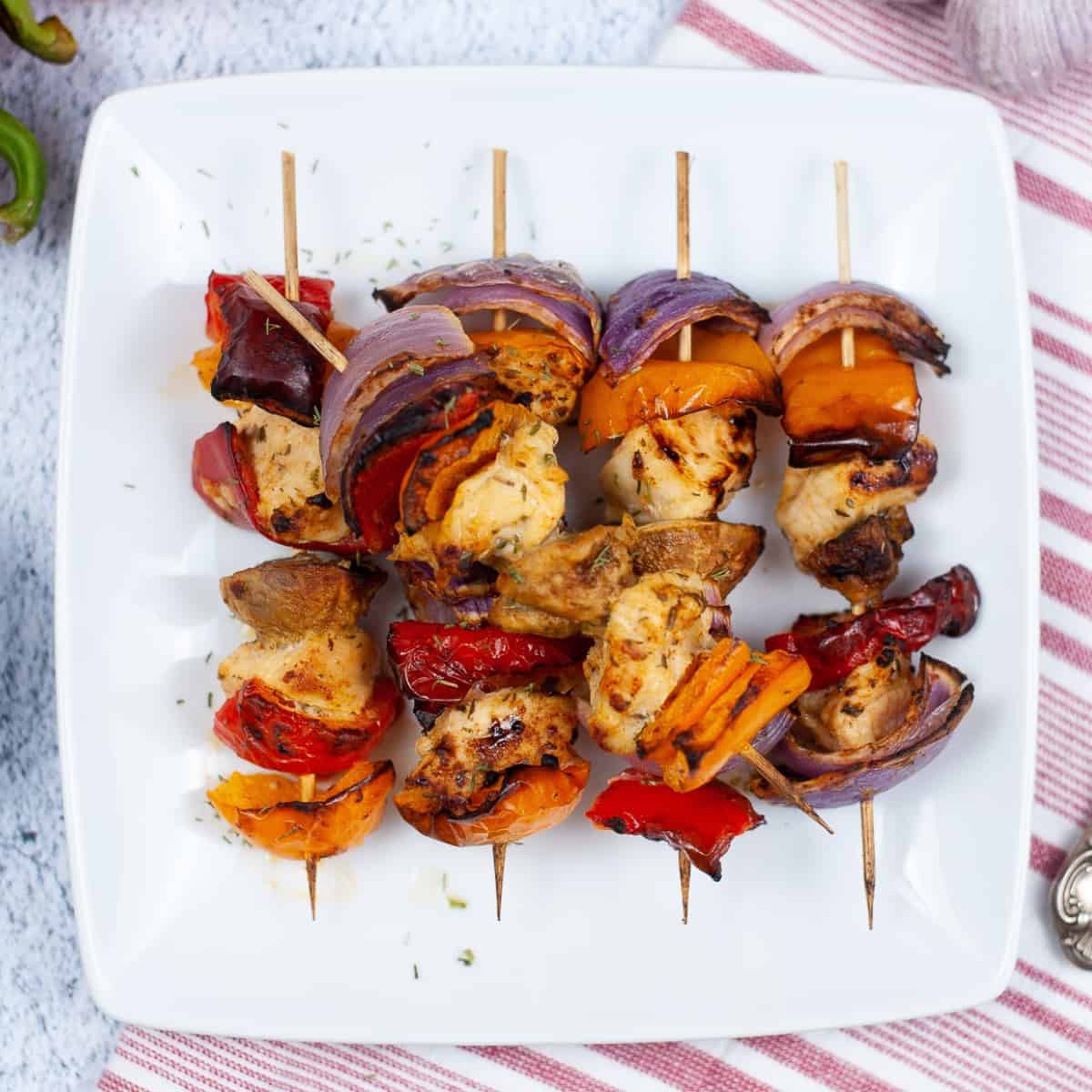 Four Greek chicken kabobs on a white plate.