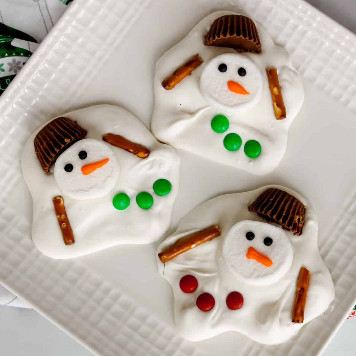 White plate of candy bark that looks like melted snowmen.