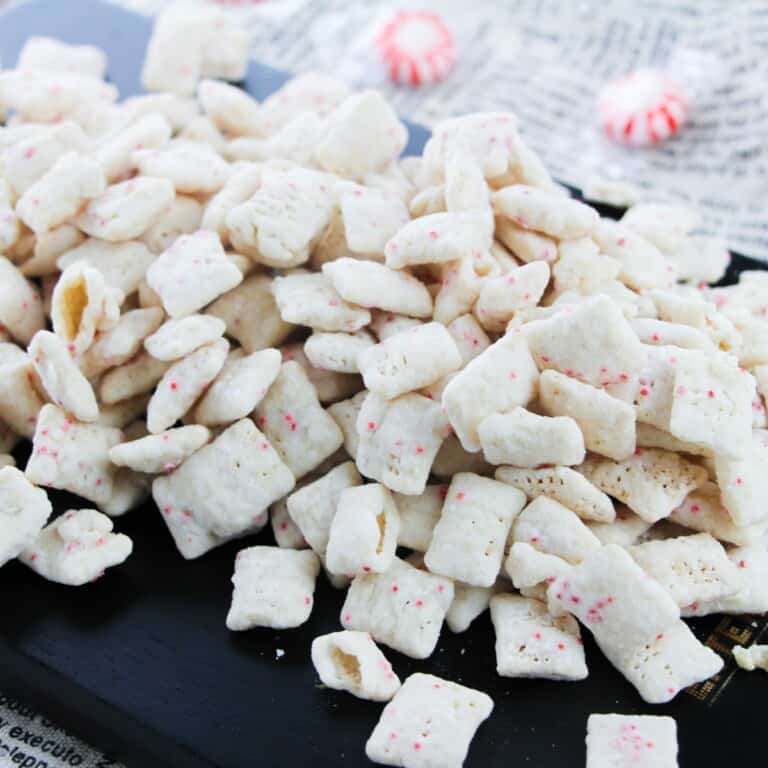 Chex cereal covered with melted peppermint bark and powdered sugar on a black plate.