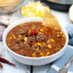 Taco soup in a white bowl with a chip on the side.