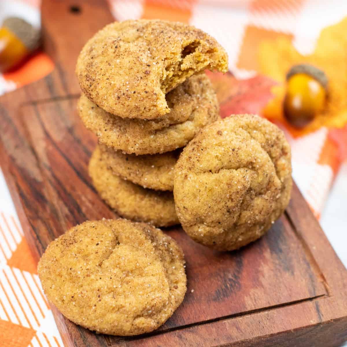 Pumpkin cookies stacked on a wooden board.