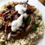 Shredded chicken with beans and sauce over rice, topped with cilantro lime sauce.