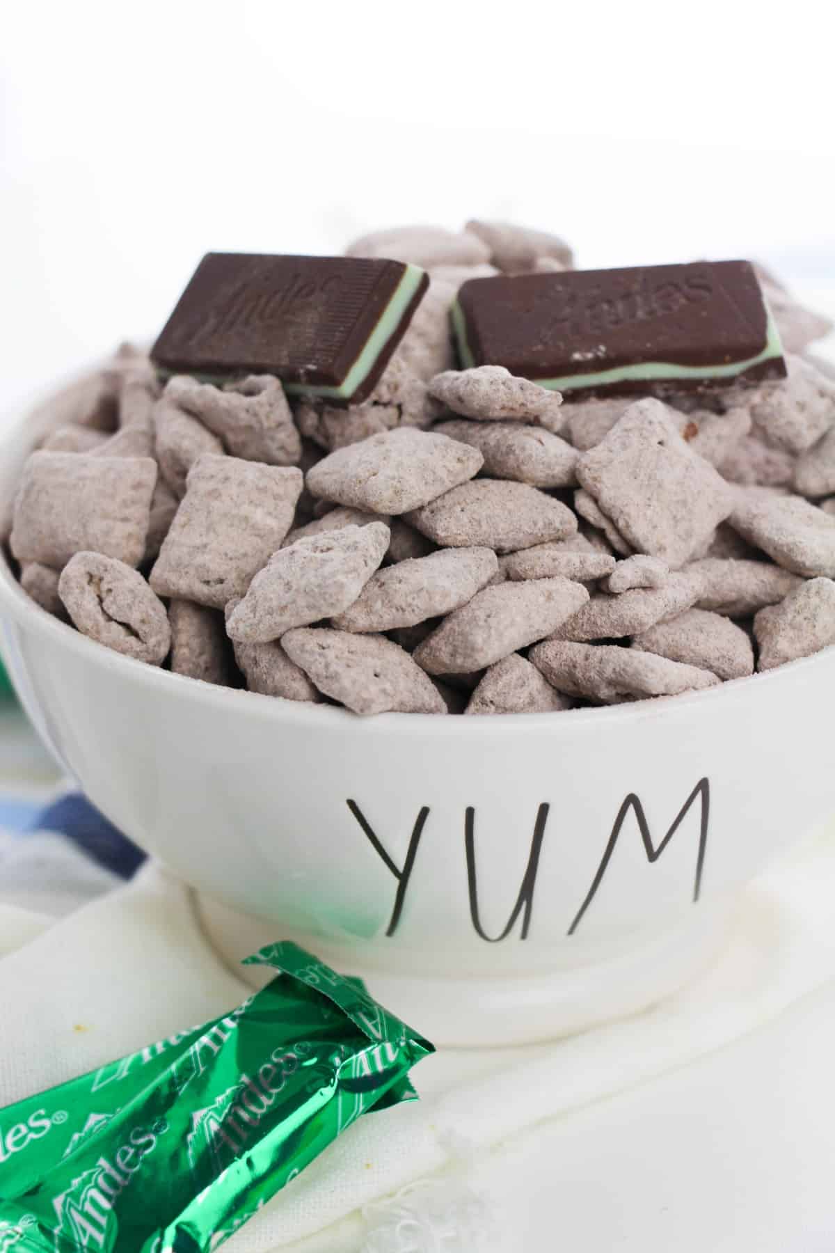 Chex cereal coated with Andes chocolate and powdered icing sugar on a white bowl topped with Andes mint chocolates.
