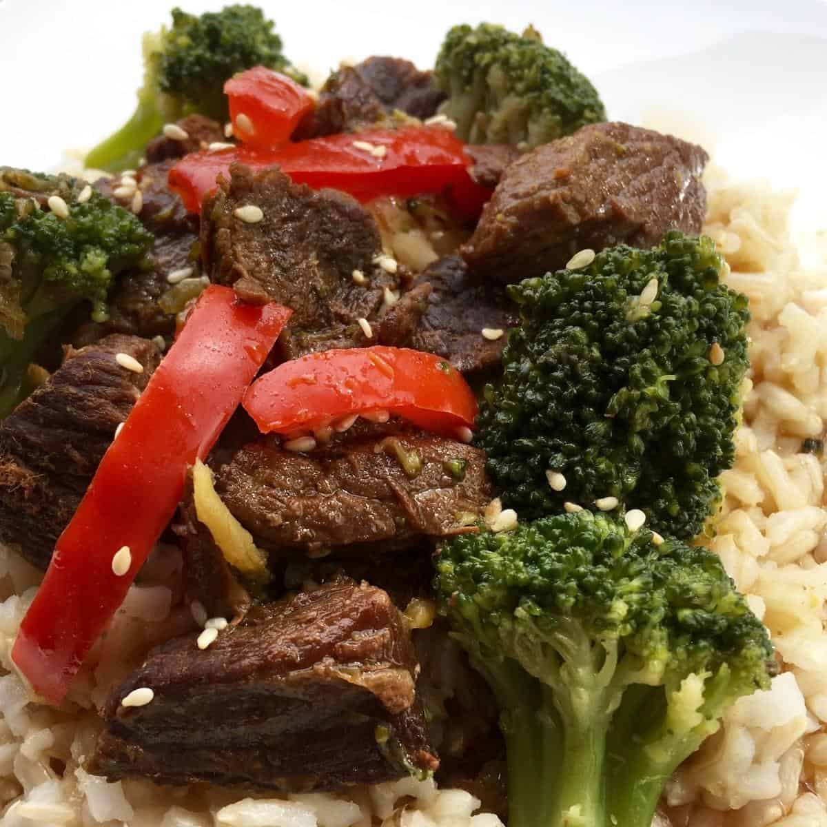 Beef with broccoli and red bell pepper on a bed of rice.