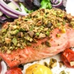 Salmon topped with chopped pistachios on a plate with blistered cherry tomatoes.
