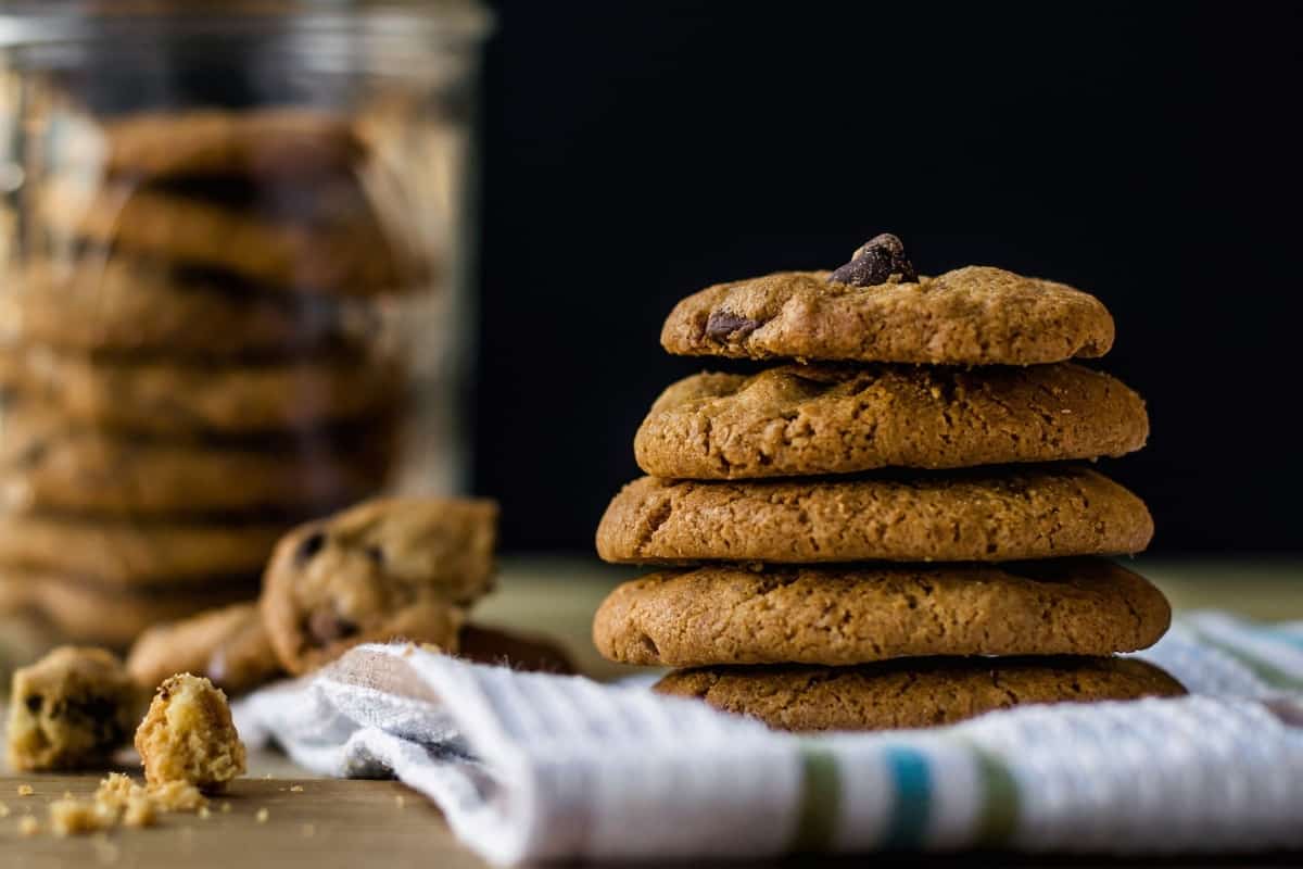 Chocolate chip cookies with cookie crumbs sitting on a wooden table.