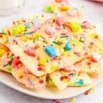 White plate with chocolate barks topped with lucky charms marshmallows and sprinkles.