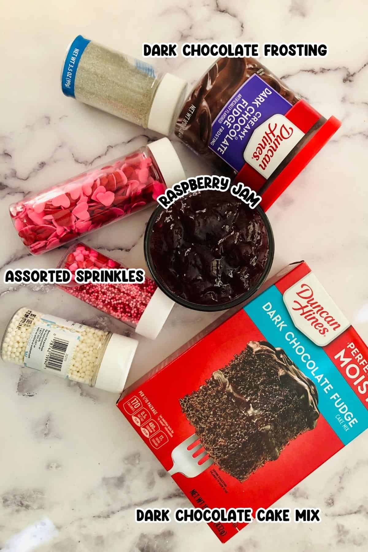 Dark chocolate frosting, raspberry jam. assorted sprinkles, and cake chocolate cake mix sitting on a countertop.
