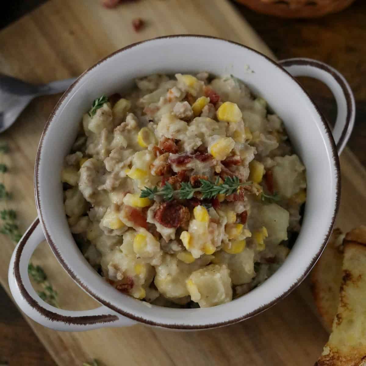 Spoon in Sausage Corn Chowder topped with Sausage and thyme in a white cooking pot.