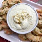 A white bowl of roasted garlic dip with shrimps on the side.