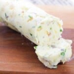 Partially-sliced roll of compound garlic butter on a wooden board.