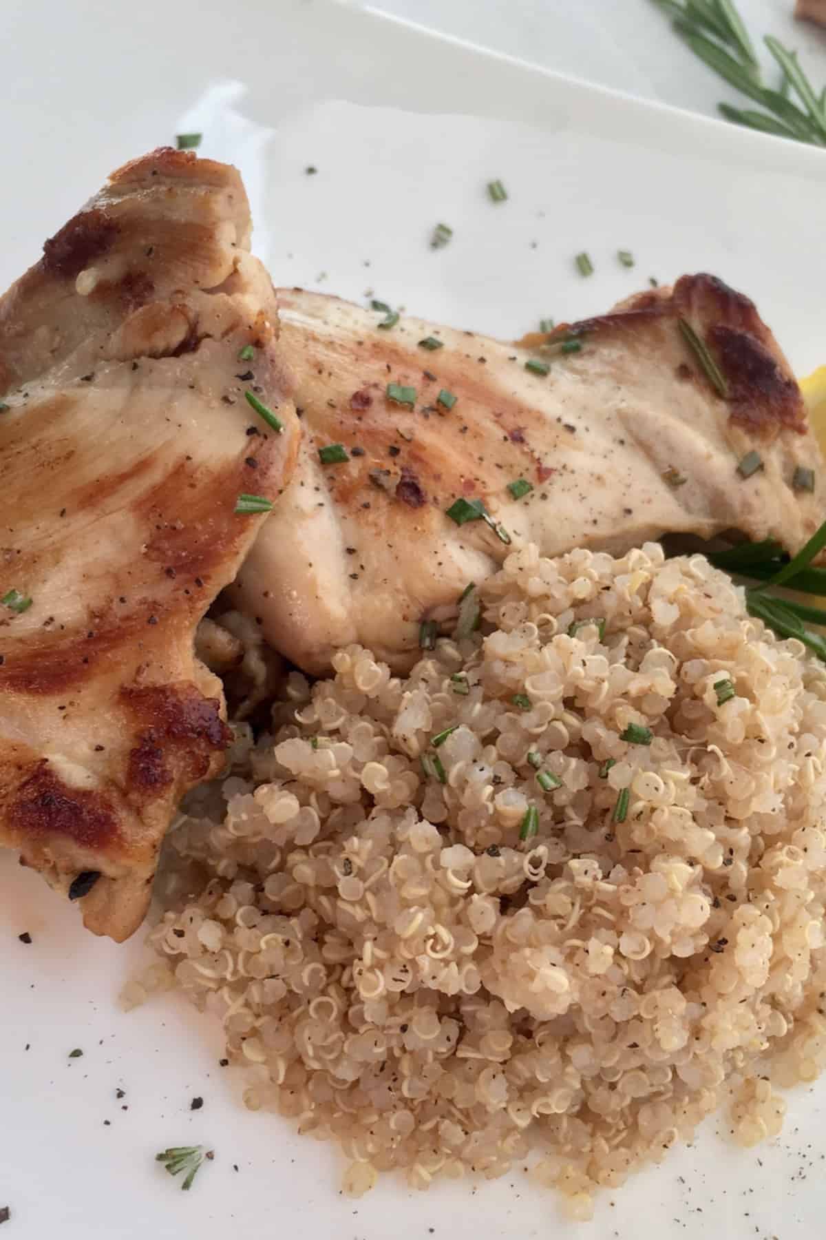 A white plate of chicken thighs with quinoa on the side.