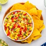Colorful pineapple Salsa on a white plate with tortilla chips on the side.