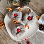 A white plate of three chocolate reindeer donuts sitting on a wooden table.