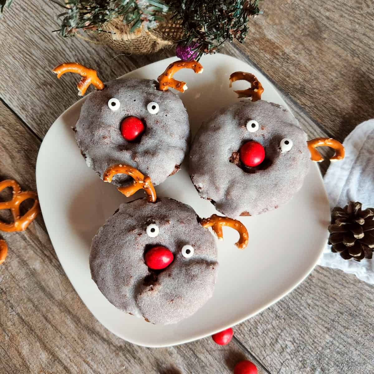 A white plate of three chocolate reindeer donuts sitting on a wooden table.