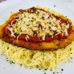 Baked chicken topped with marinara sauce and melted mozzarella cheese on a plate with pasta.