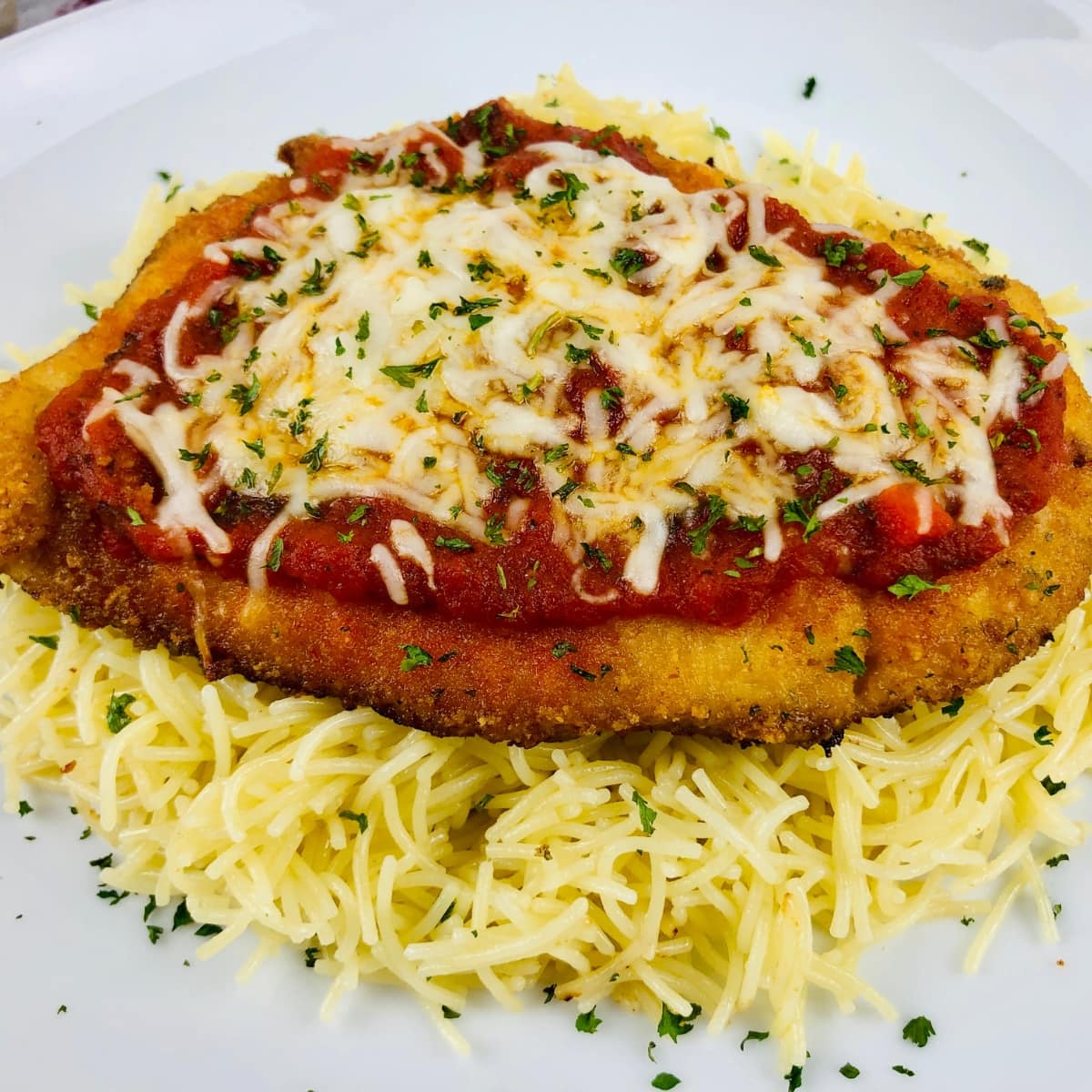 Baked chicken topped with marinara sauce and melted mozzarella cheese on a plate with pasta.