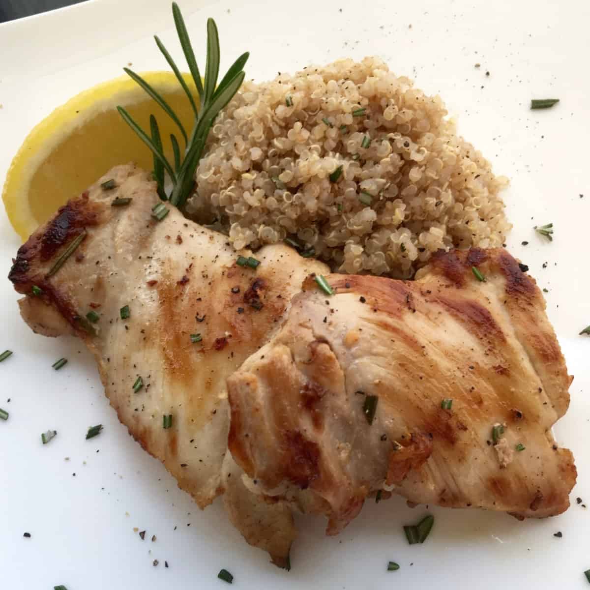 Plate of Chicken Thighs with rosemary and sliced lemon on the side.