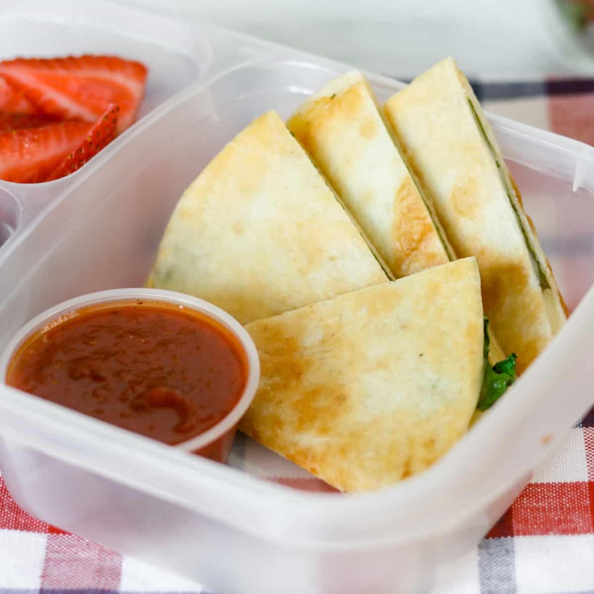 Lunch container of spinach pizzadillas with marinara.