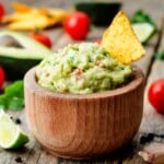 Wooden bowl of mango habanero Guacamole with a chip sticking out.