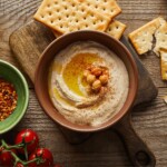 Wooden bowl of Hummus Dip surrounded by crackers.