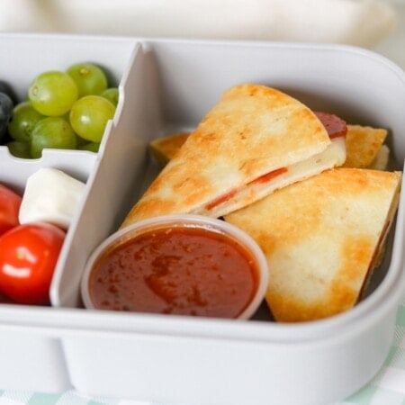 Pepperoni Pizzadilla in lunchbox with grapes, blueberries, and tomatoes.