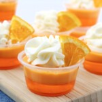 Orange jello shots topped with whipped cream and orange slices.