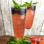 Two glasses of cocktail garnished with blackberries and basil.
