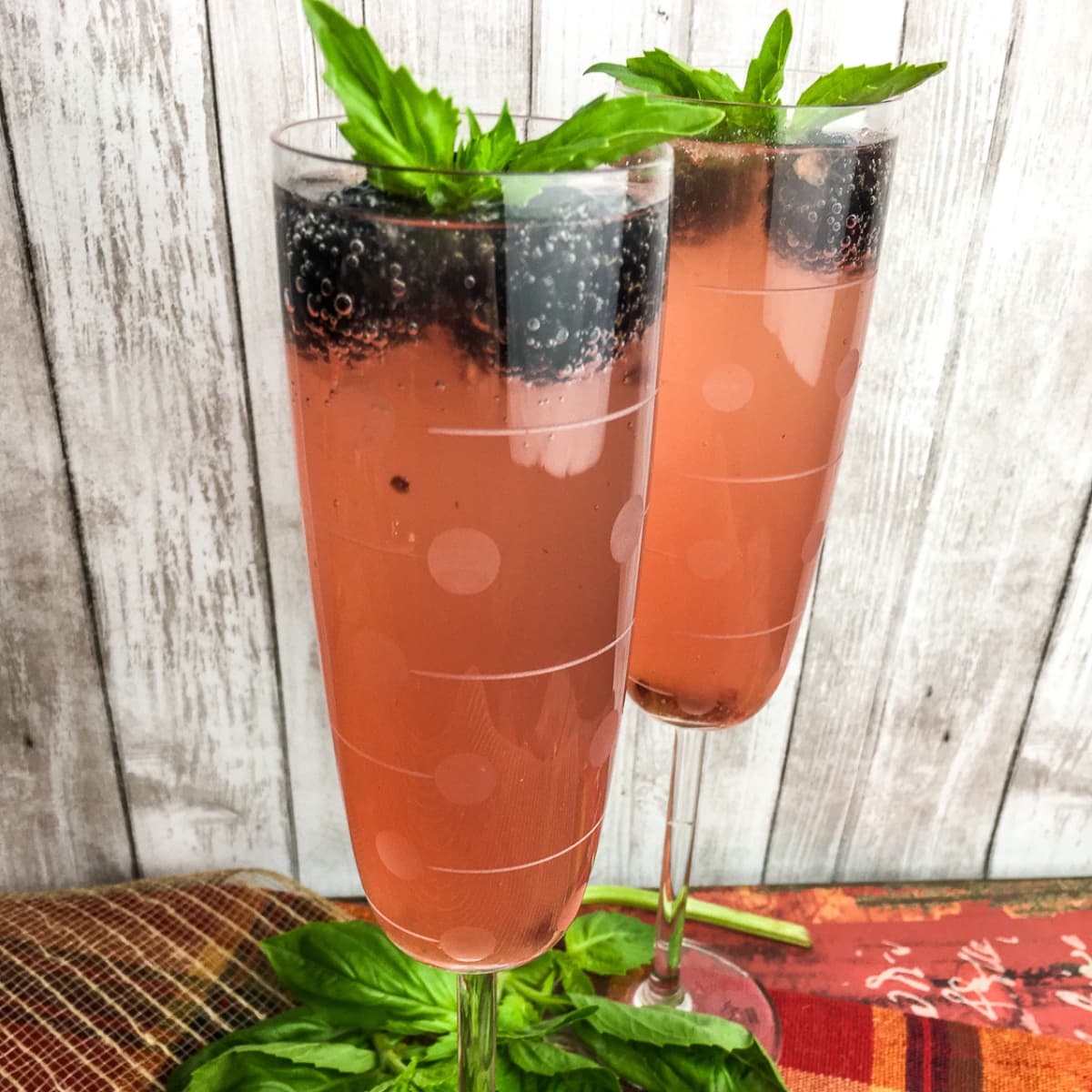 Two glasses of cocktail garnished with blackberries and basil.
