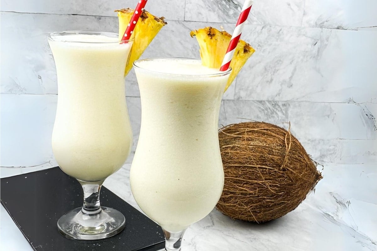 Frozen Pina Coladas with red straw and pineapple wedge on the rim.