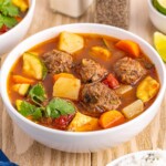 Mexican Meatball Soup in a white bowl sitting on a wooden table.