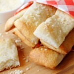 Baked breadsticks topped with parmesan sitting on a wooden cutting board.