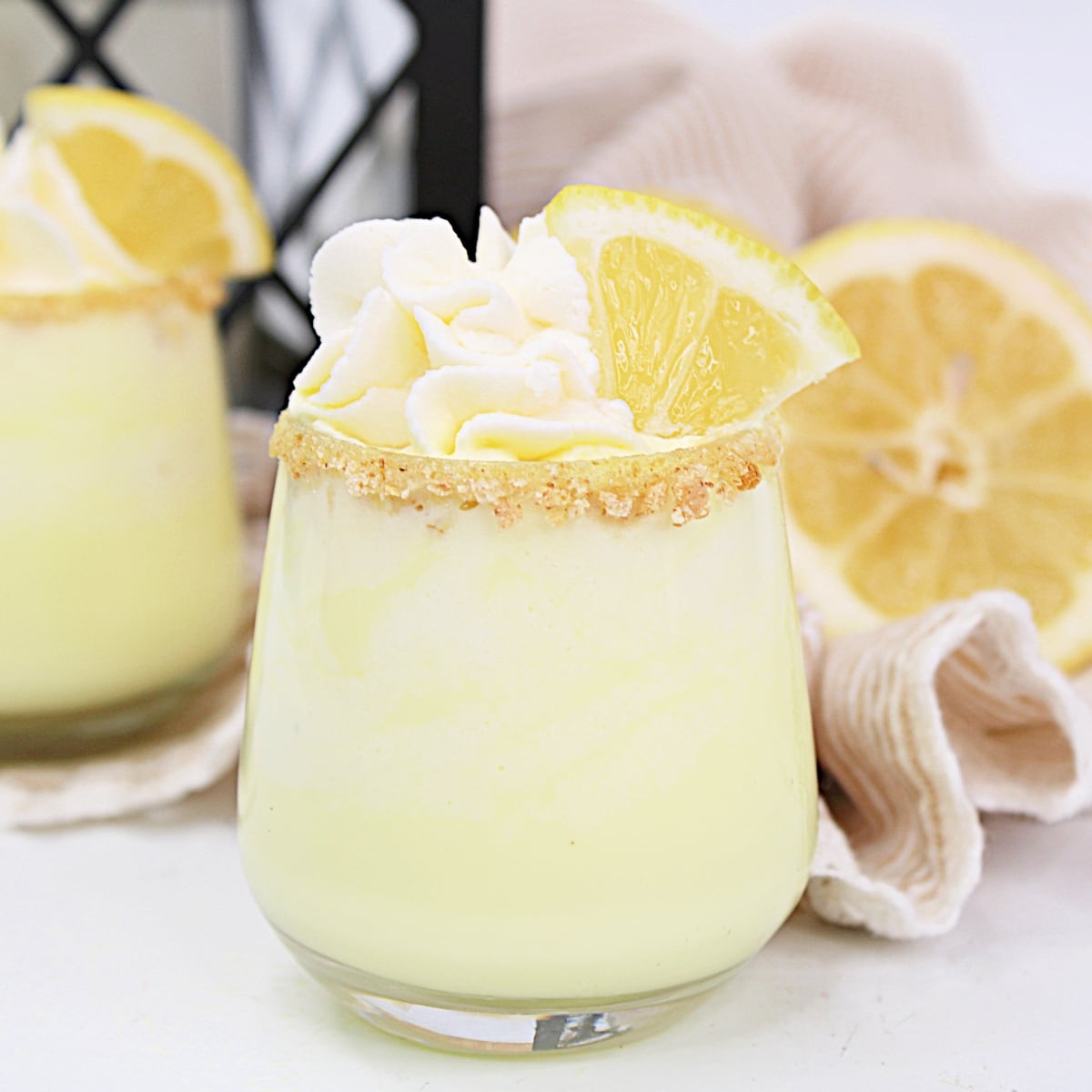 Lemon Meringue Shot with whipped cream and a lemon wedge sitting on a white countertop.