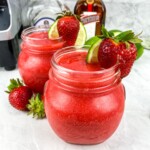 Strawberry Margaritas in glass jars with strawberries and limes on the rims.