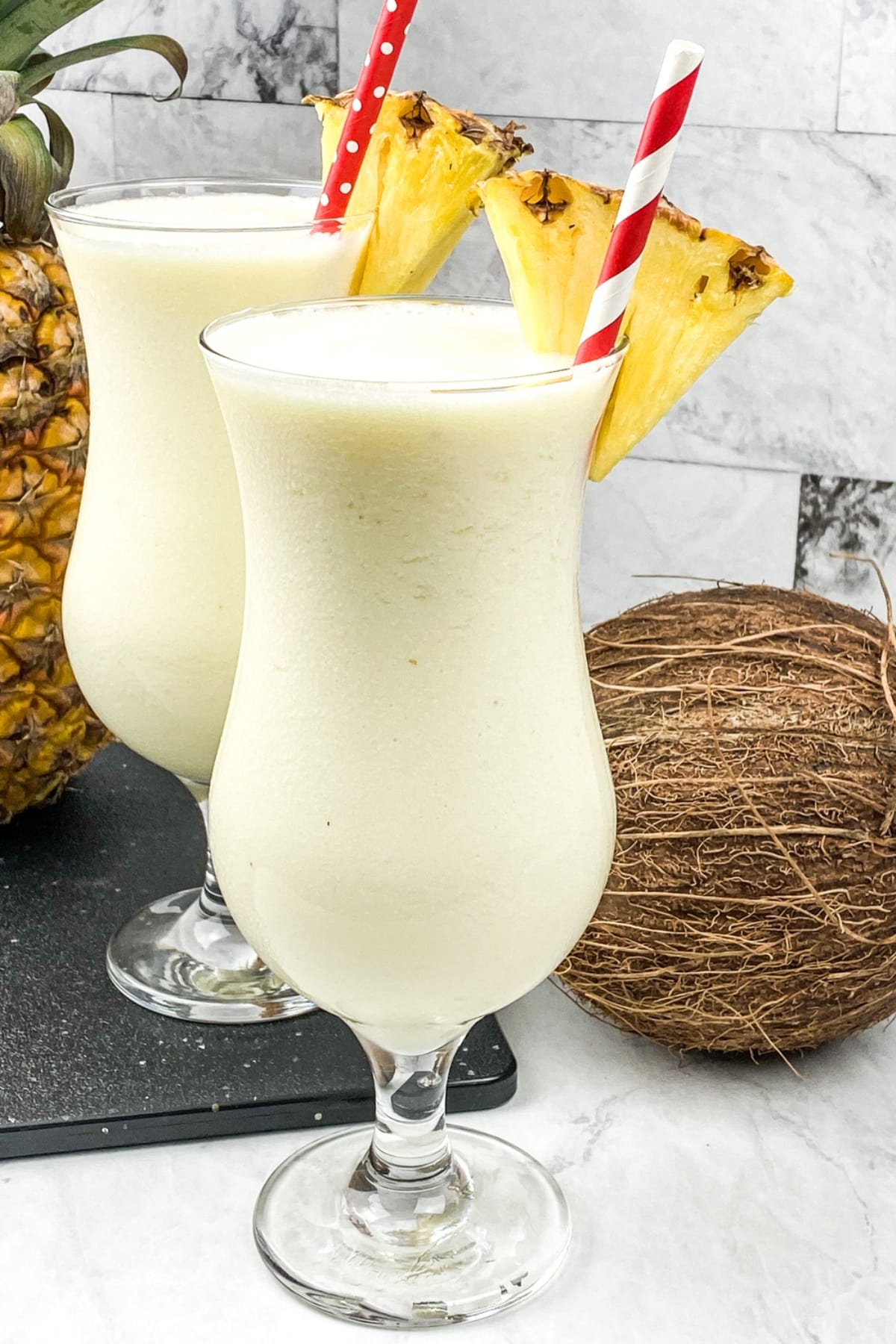 Two tall glasses of Frozen Pina Colada with coconut and pineapple on the side.