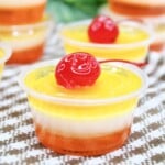 Pina Colada jello shots with cherries on top in small plastic cups.