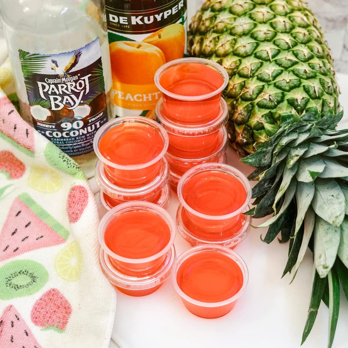 Condiment cups of Jello with pineapple, Coconut Rum and Peach Schnapps sitting on the countertop.