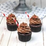 Three Dr. Pepper Cupcakes with chocolate frosting sitting on a wooden table.
