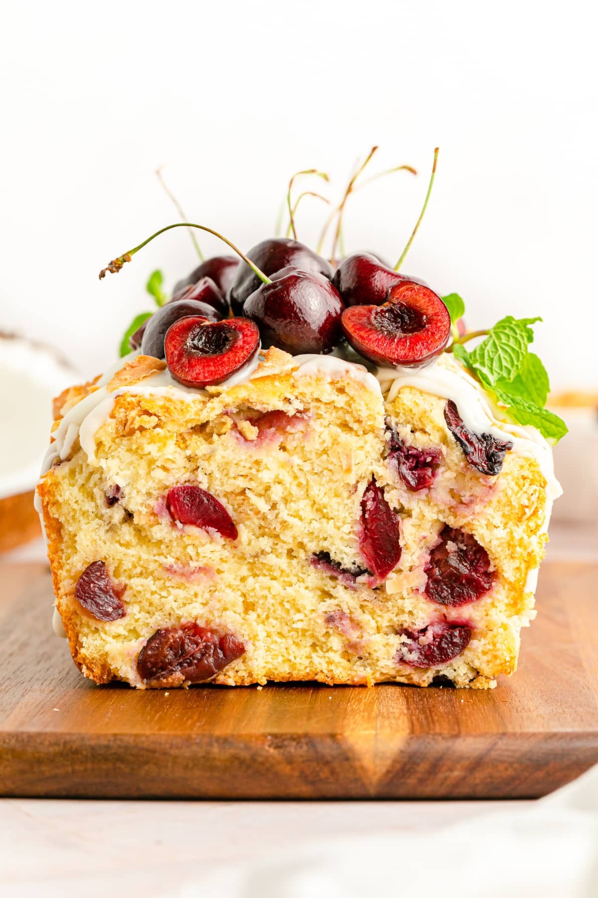 Cherry Loaf on a wooden surface and topped with glaze, fresh cherries and mint leaves.