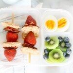 Sectioned lunch box with Mini Waffle Skewers, kiwi, blueberries, and hard boiled eggs.